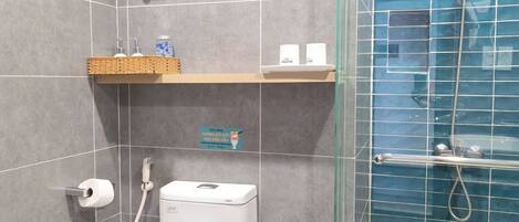 A bathroom with a toilet, a bidet, a glass shower enclosure, and a trash bin.