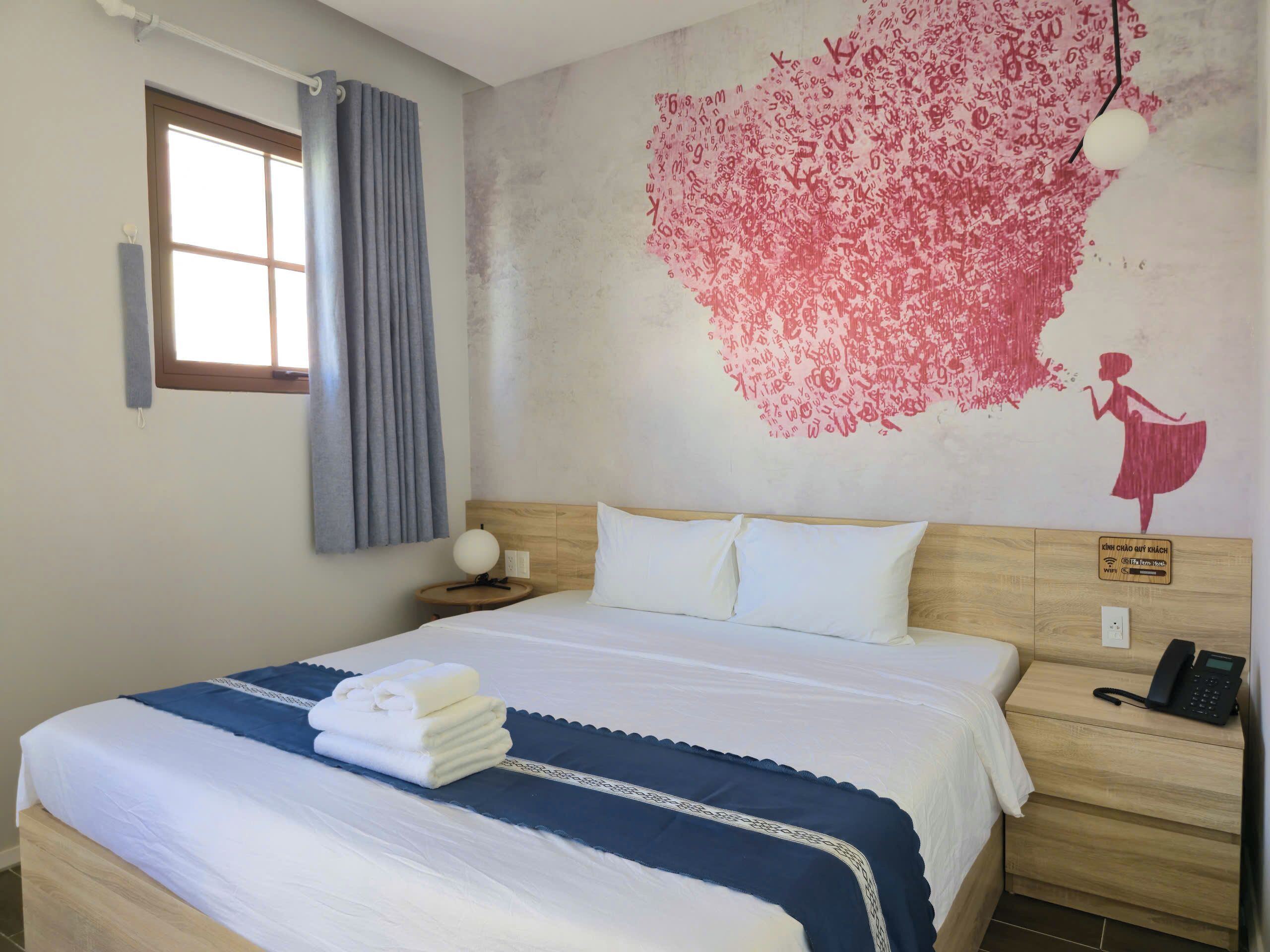 Une chambre d’hôtel comprenant un lit, une table de chevet, une horloge murale, une fenêtre avec des rideaux et un élément décoratif mural.