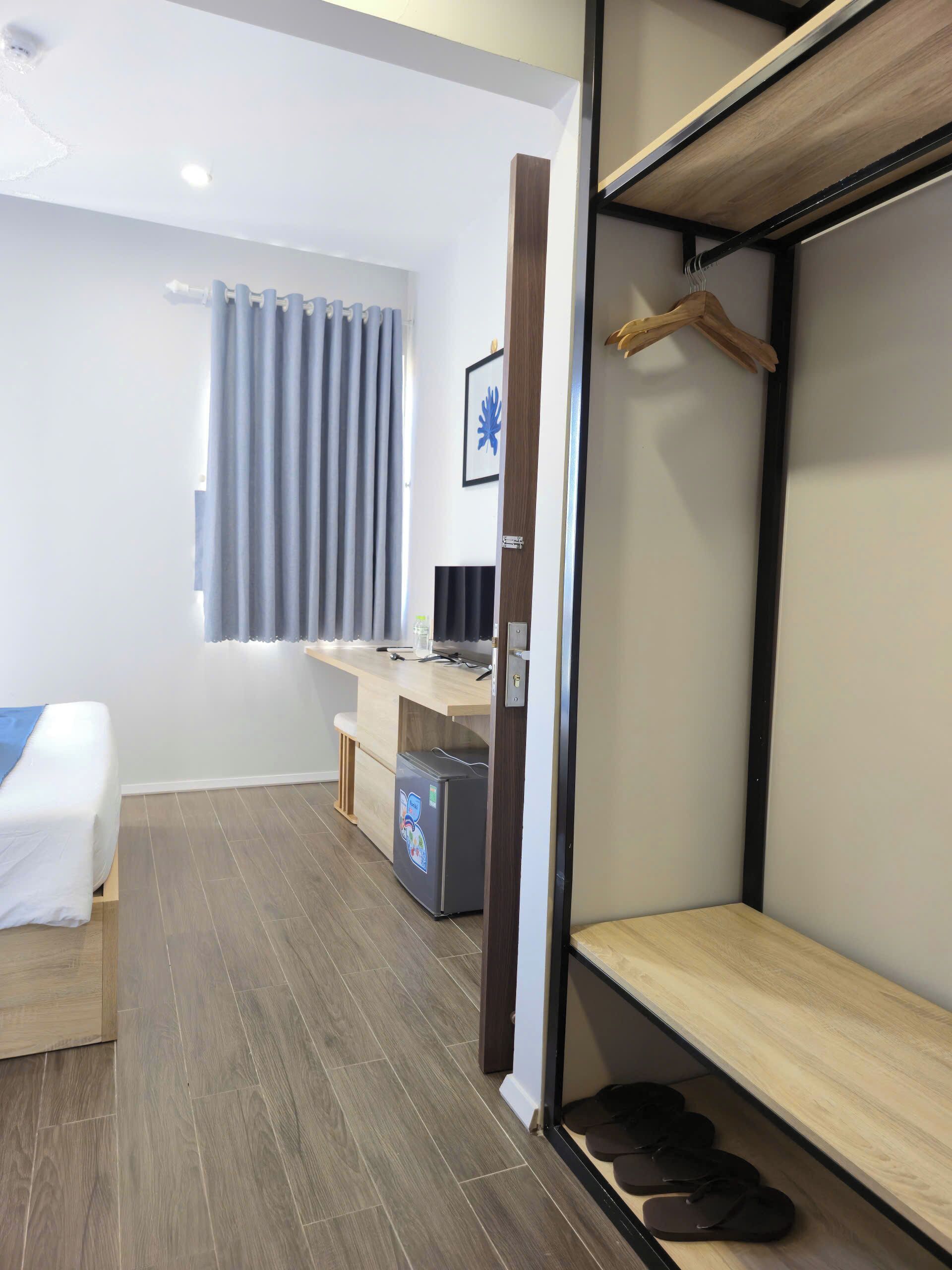 Habitación de hotel compacta con cama, escritorio, refrigerador pequeño y zapatero.