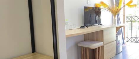 Una sala moderna con piso de madera, un estante de metal negro, una pared blanca con un cuadro enmarcado, un taburete de madera y una ventana con cortinas.