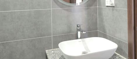 Un baño con encimera de granito, un lavabo blanco, un espejo redondo y un secador de pelo fijado en la pared.