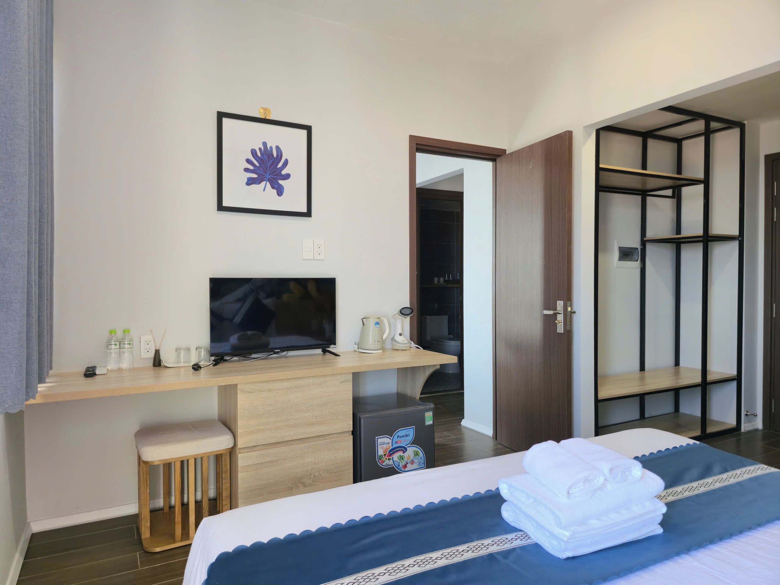 A hotel room with a bed, a desk with a TV, a minibar, and a wardrobe.
