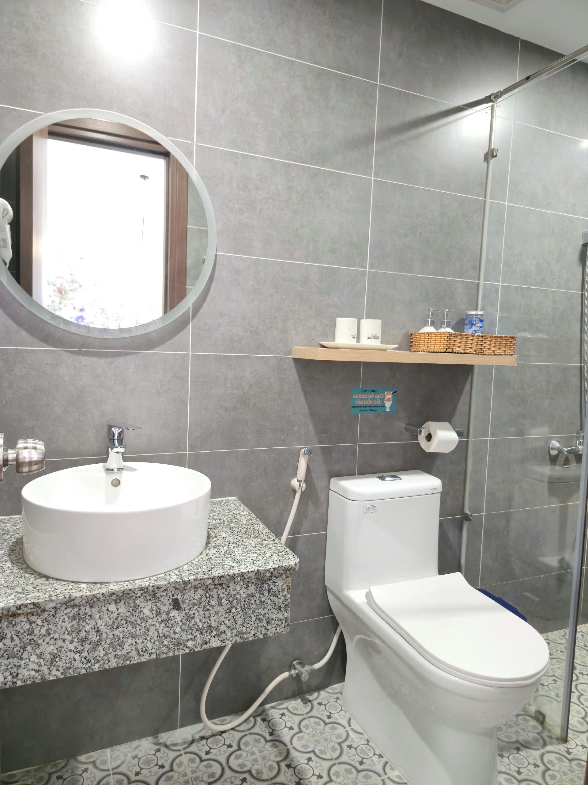 A bathroom with a round mirror, a sink with a faucet, a toilet, and a shower area.