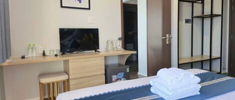 Ein Hotelzimmer mit Bett, Schreibtisch mit Fernseher, Kleiderschrank und einem durchgegangene Tür erkennbaren Badezimmer.