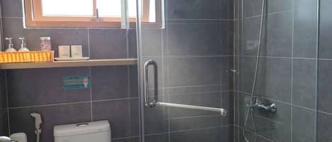A modern bathroom with a glass-enclosed shower, a toilet, and a sink area with toiletries.