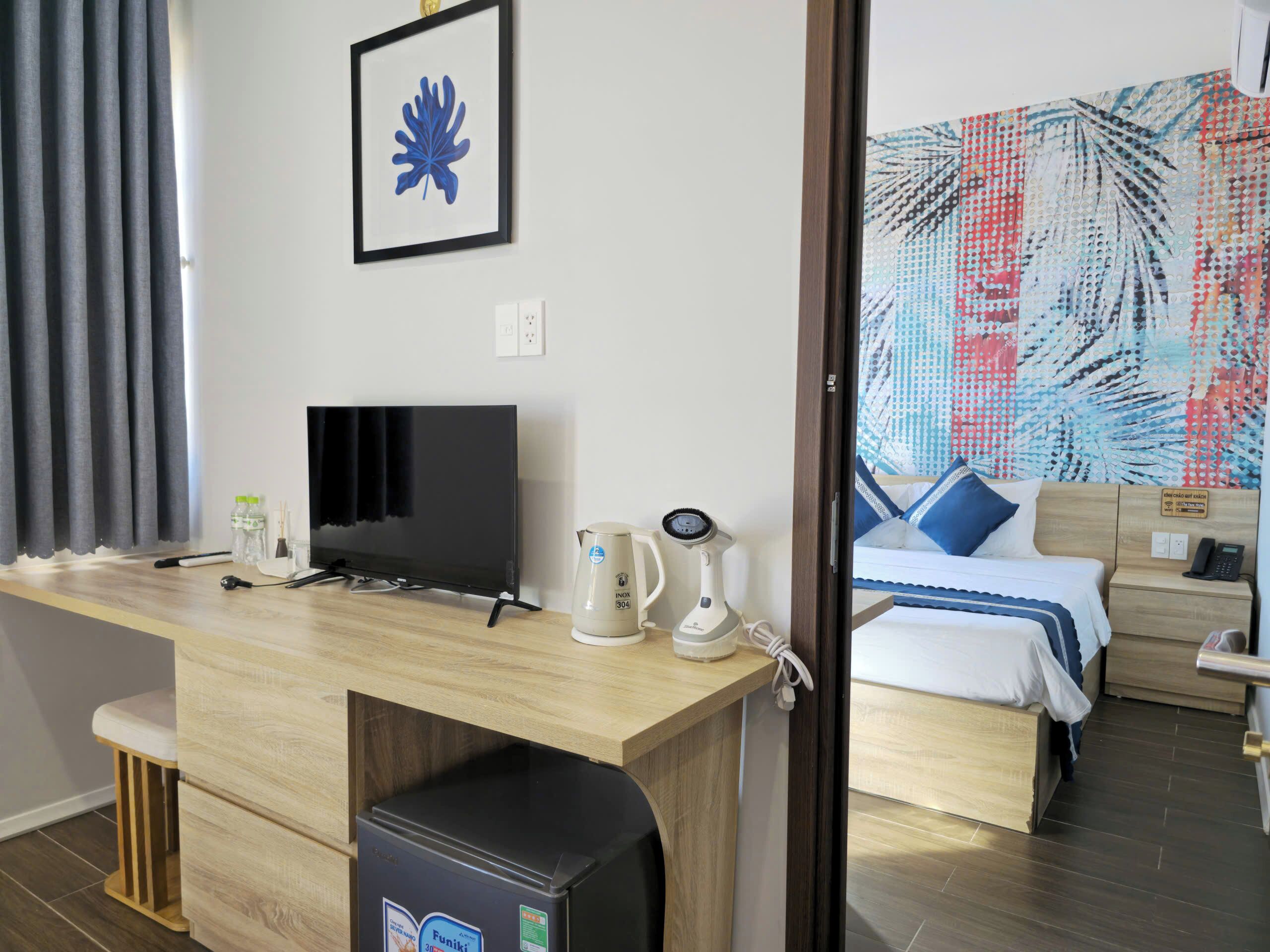 A hotel room with a wooden desk, a television, a kettle, and a bed with a patterned bedspread.