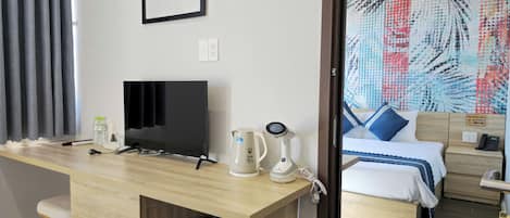 A hotel room with a wooden desk, a television, a kettle, and a bed with a patterned bedspread.