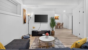 A modern living room with a flat-screen TV, sofa, coffee table, and a dining area with chairs. - Spacious 2 bedroom unit in North Edmonton. (Edmonton)