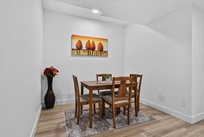 A dining area with a wooden table and chairs, a vase with flowers, and a painting on the wall.