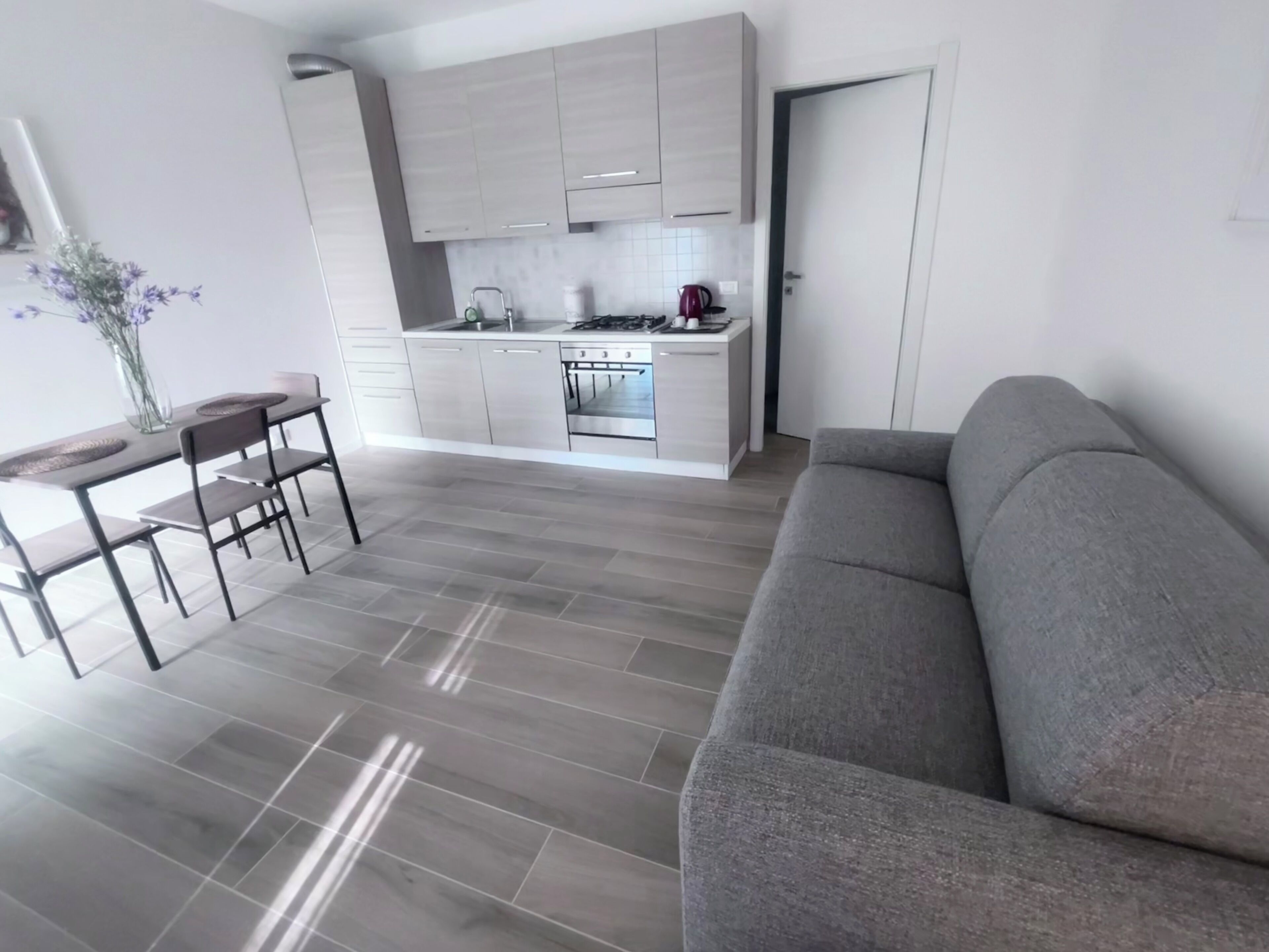 Eine moderne Küche mit grauen Schränken, ein Essbereich mit Tisch und Stühlen sowie ein graues Sofa im Wohnbereich.