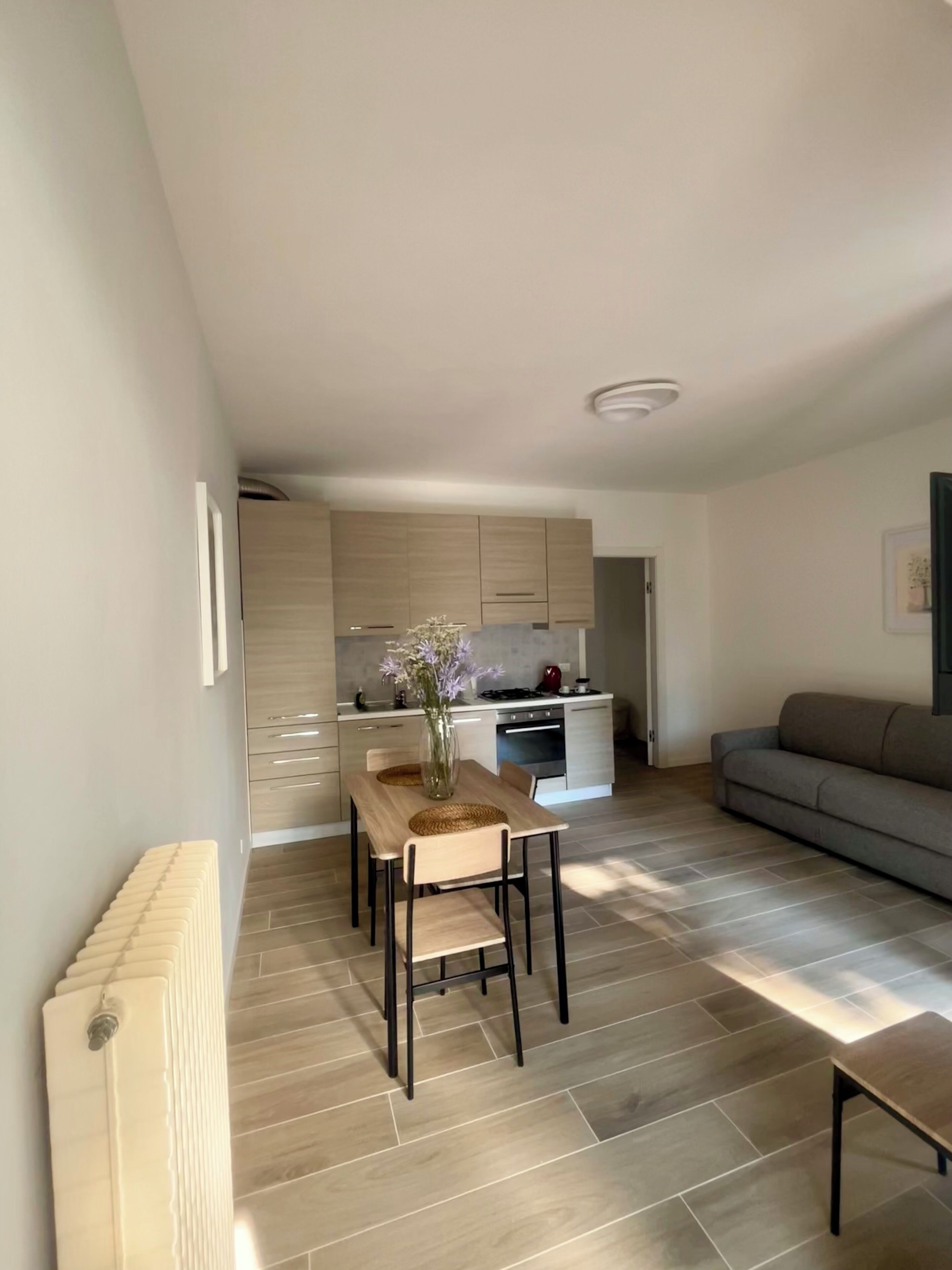 A modern kitchen with wooden cabinets, a dining table with chairs, and a gray sofa in a living area.