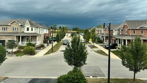 Une rue de banlieue bordée de maisons à deux étages, une route dégagée et un ciel orageux.