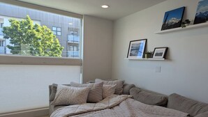 A bedroom with a large bed, a window with blinds, and a wall with framed pictures.