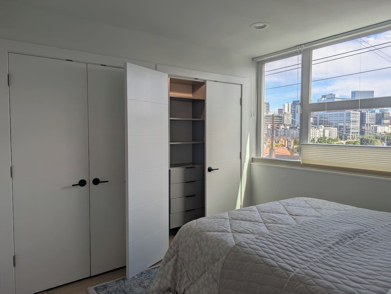 Een slaapkamer met een bed, een kast met verschillende vakken en een raam met uitzicht over de stad.