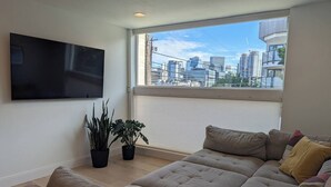 A modern living room with a large window, a flat-screen TV, and a sectional sofa.