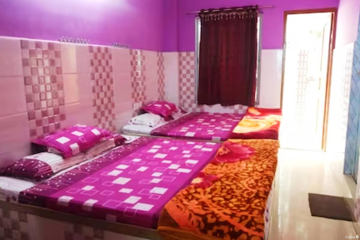A room with two beds, each with a patterned bedspread. The walls have a checkered pattern, and there is a window with a curtain.