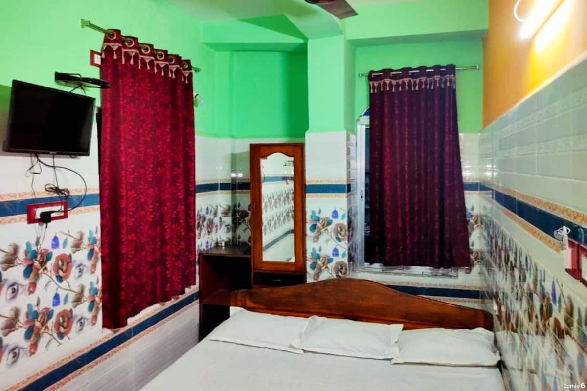 A small, brightly colored room with a bed, a ceiling fan, a television mounted on the wall, and a mirror.