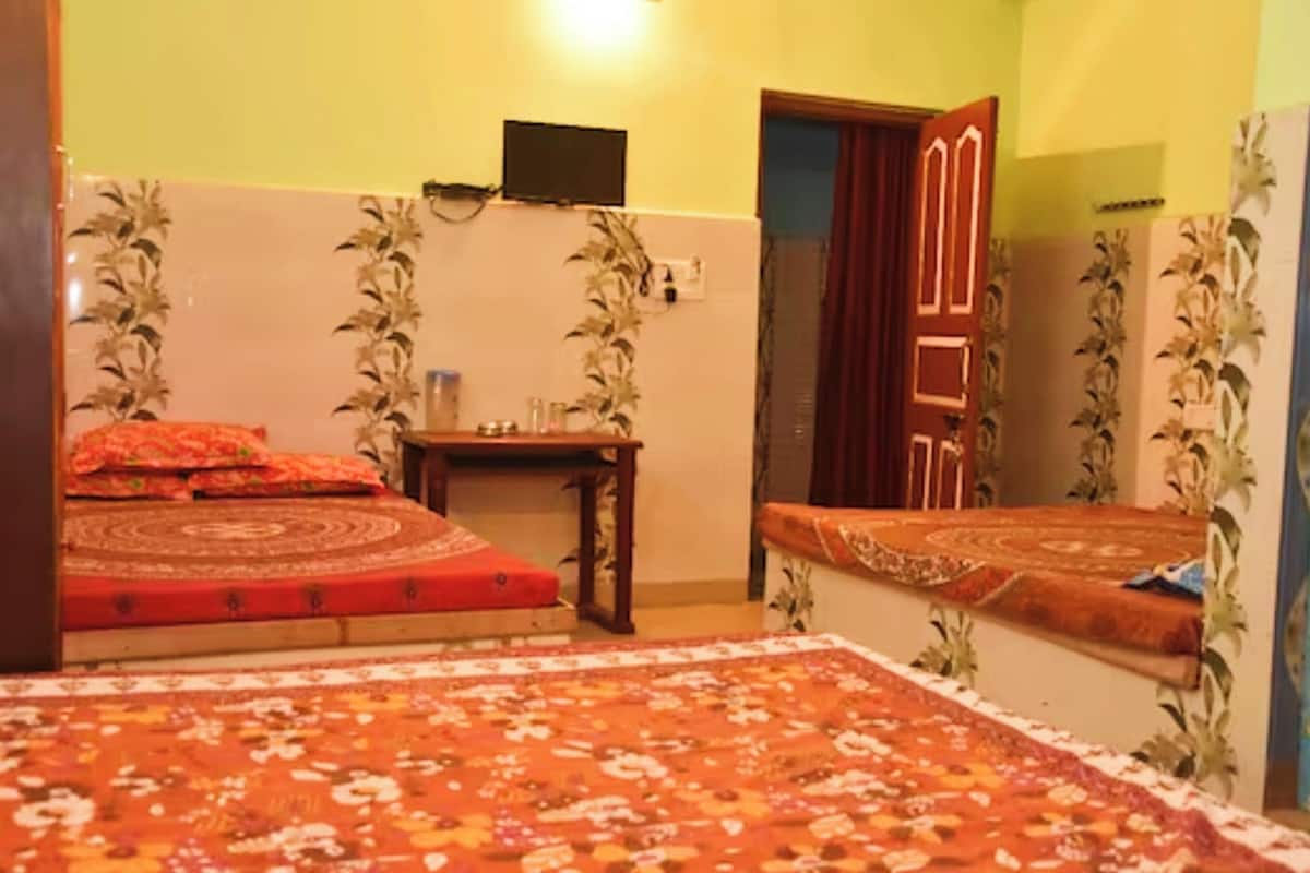 A room with two beds, a small table, a television on the wall, and a door with a mirror.