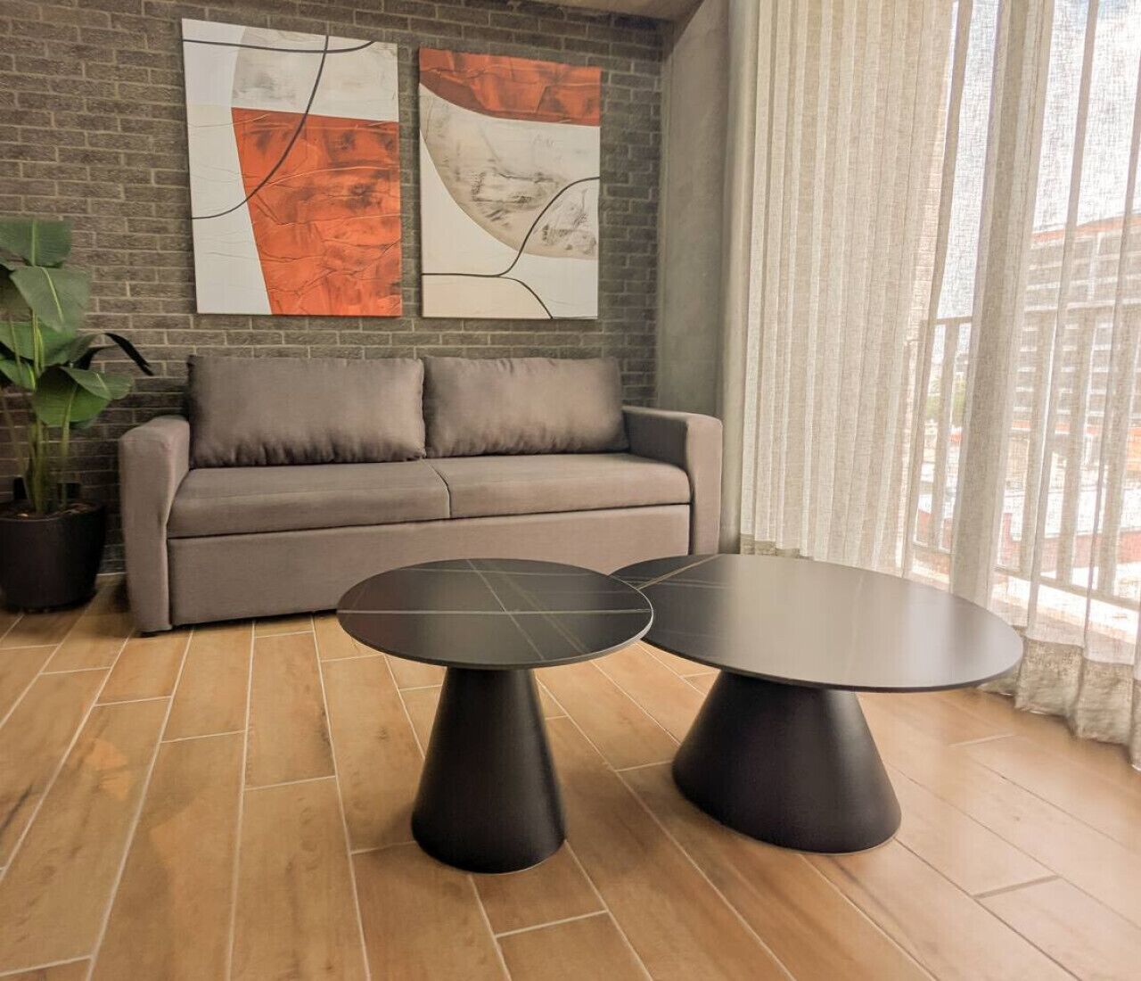 Een moderne woonkamer met een grijze bank, twee zwarte ronde tafels en abstracte kunst aan de muur.