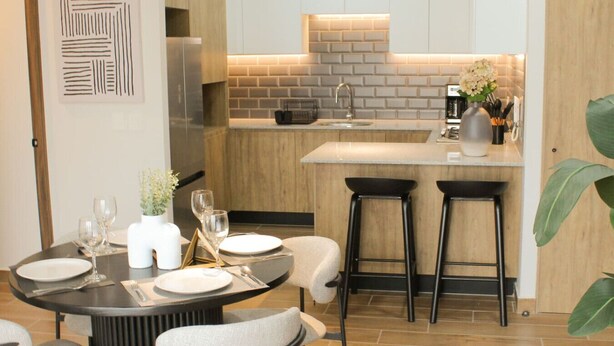 A modern kitchen with a central island, bar stools, and a dining area with a round table set for two.