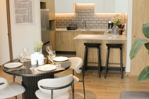 Cozinha moderna com ilha central, banquetas de bar e área de refeições com mesa redonda para dois.