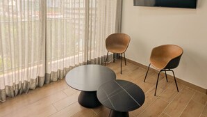 A room with two round tables, two chairs, a TV on the wall, and a view through sheer curtains.