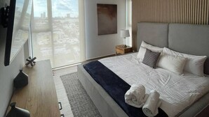 A modern hotel room with a large bed, a desk, a TV, and a city view through the window.