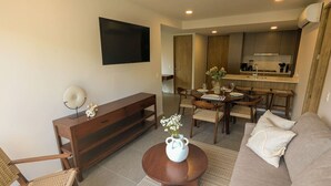 A living room with a sofa, a coffee table with a vase, a TV mounted on the wall, and a dining area with chairs and a table. - Beautiful Apartment in the Heart of Zapopan 306A (Zapopan)