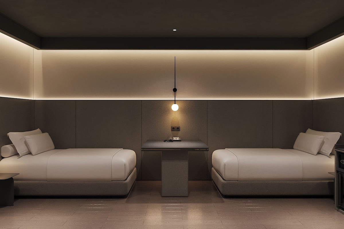 Ein modernes, minimalistisches Zimmer mit zwei Betten, einem zentralen Tisch und einer Pendelleuchte.