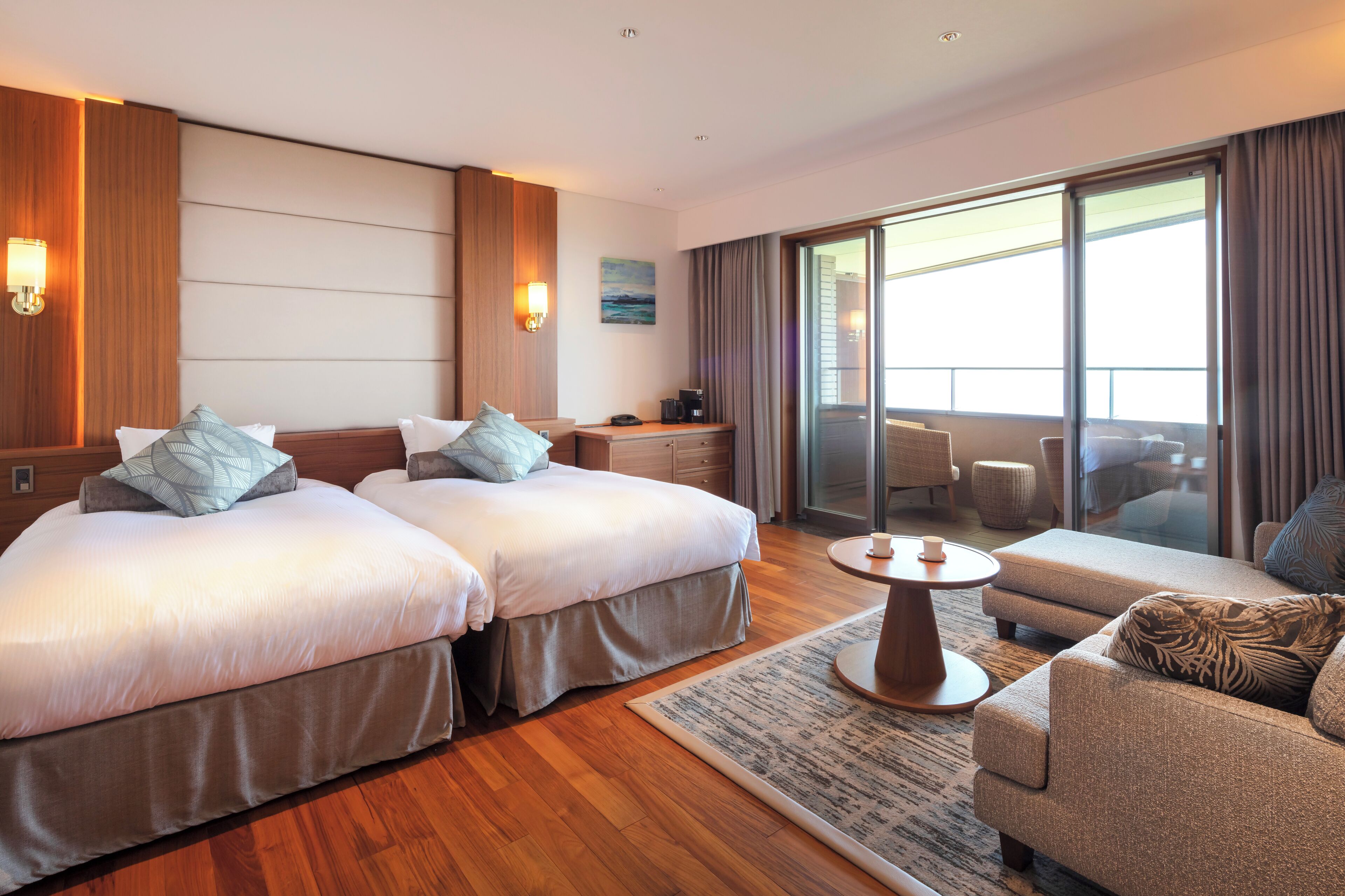 A hotel room with two beds, a sofa, a coffee table, and a view of the outside.
