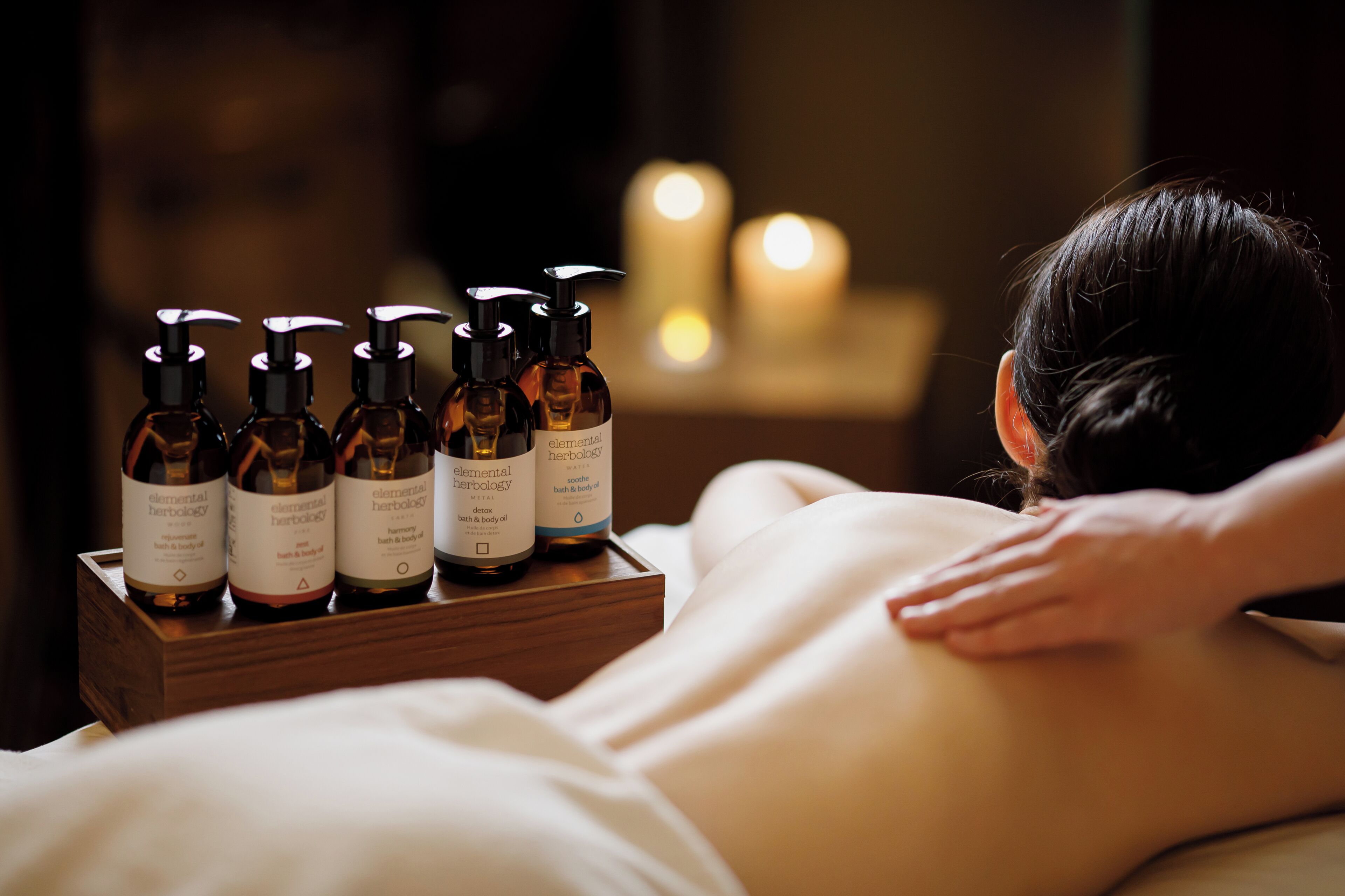 A massage therapy session with bottles of essential oils on a wooden tray.