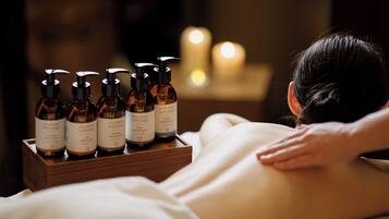 A massage therapy session with bottles of essential oils on a wooden tray.
