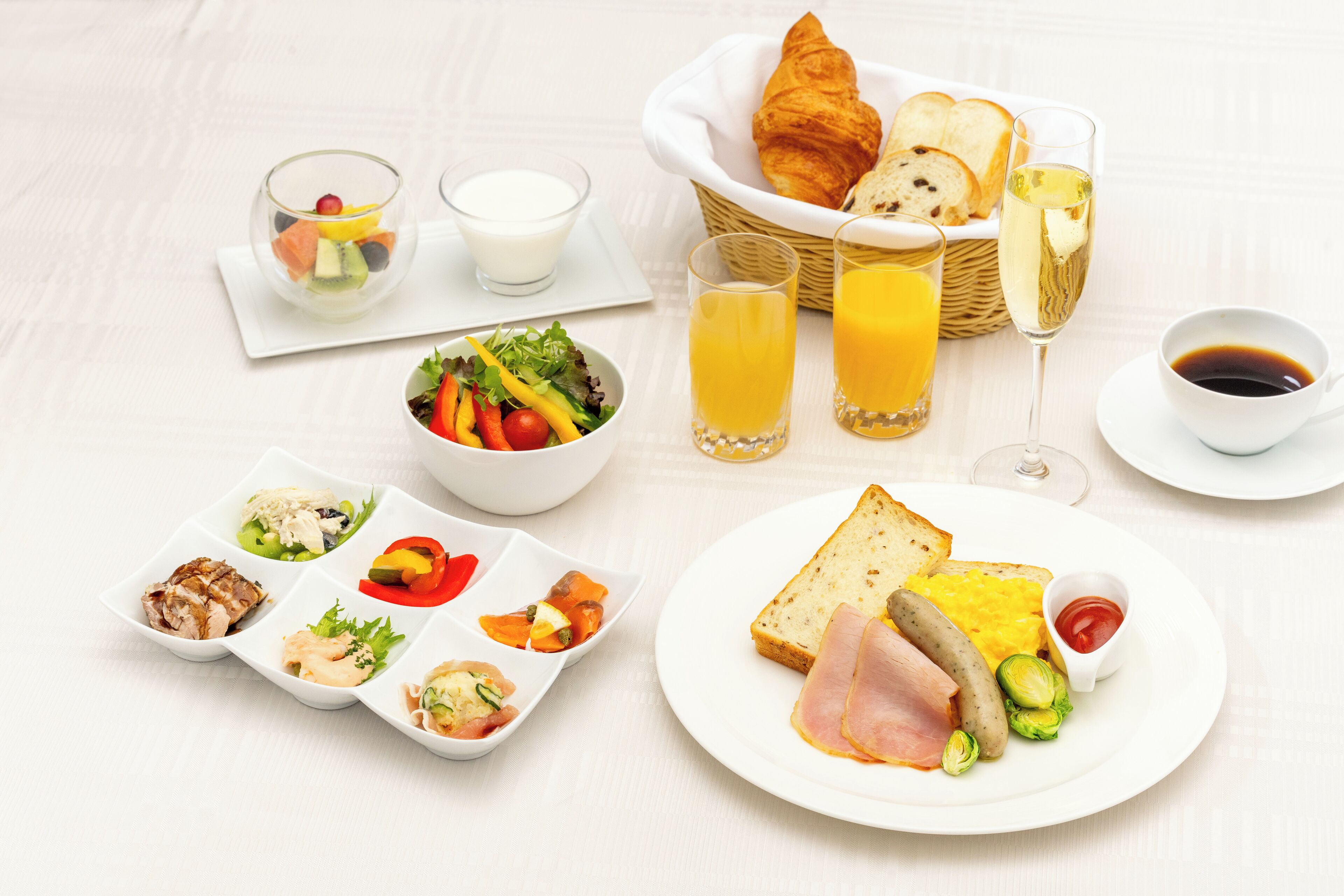 Un desayuno con cruasanes, tostadas, jamón, huevos y varios acompañamientos.