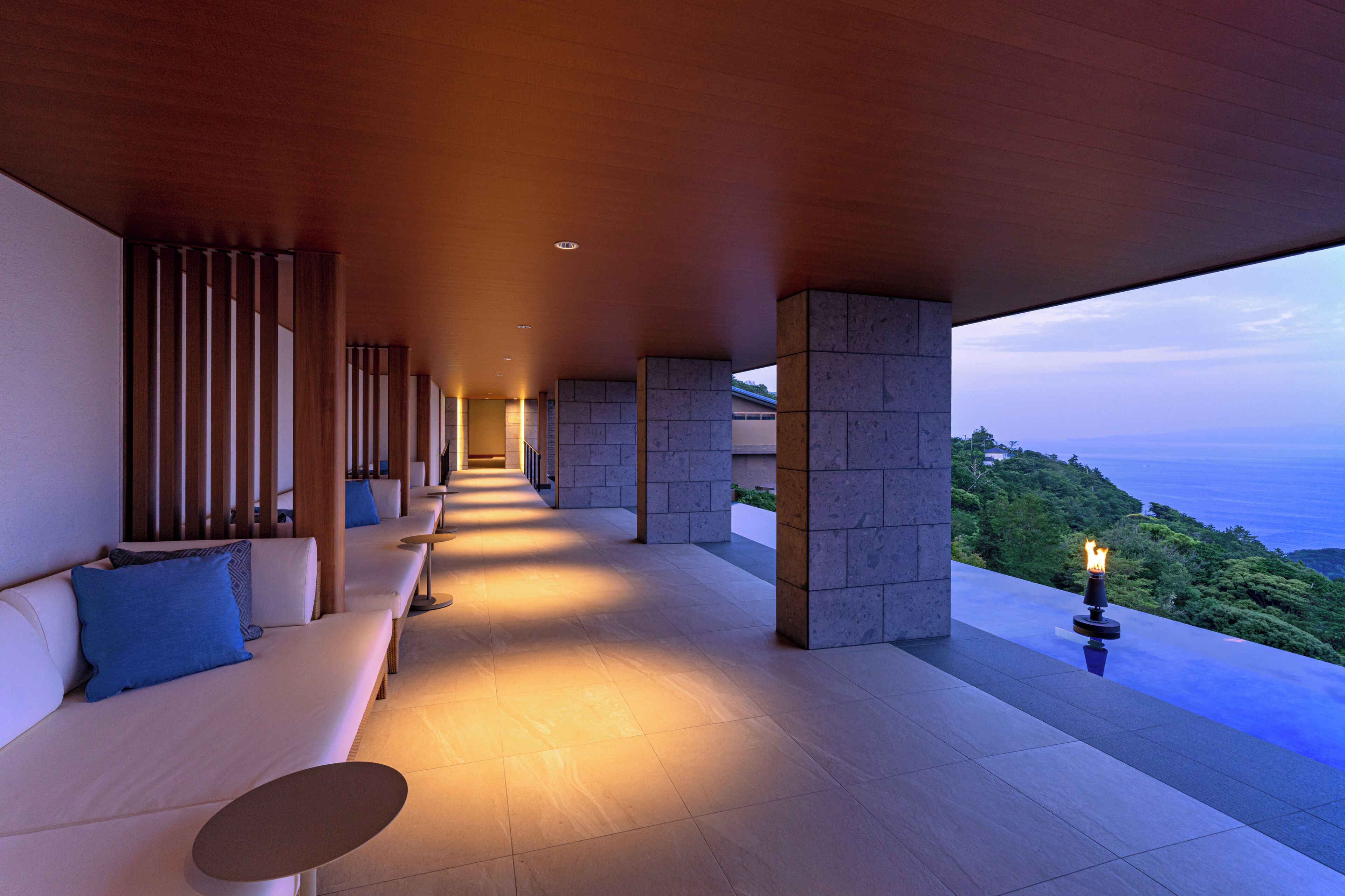 A modern outdoor lounge area with a long bench, a small table, and a view of the ocean.