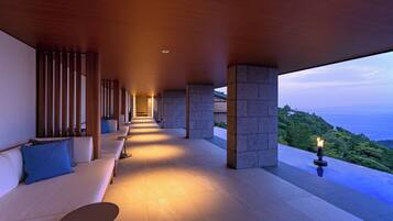 A modern outdoor lounge area with a long bench, a small table, and a view of the ocean.