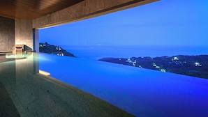 A modern infinity pool with a view of the ocean and distant lights. - Izu Hotel Resort & Spa (Higashiizu)