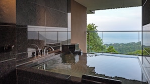 A modern bathroom with a large bathtub, a glass-enclosed shower area, and a view of the ocean. - Izu Hotel Resort & Spa (Higashiizu)