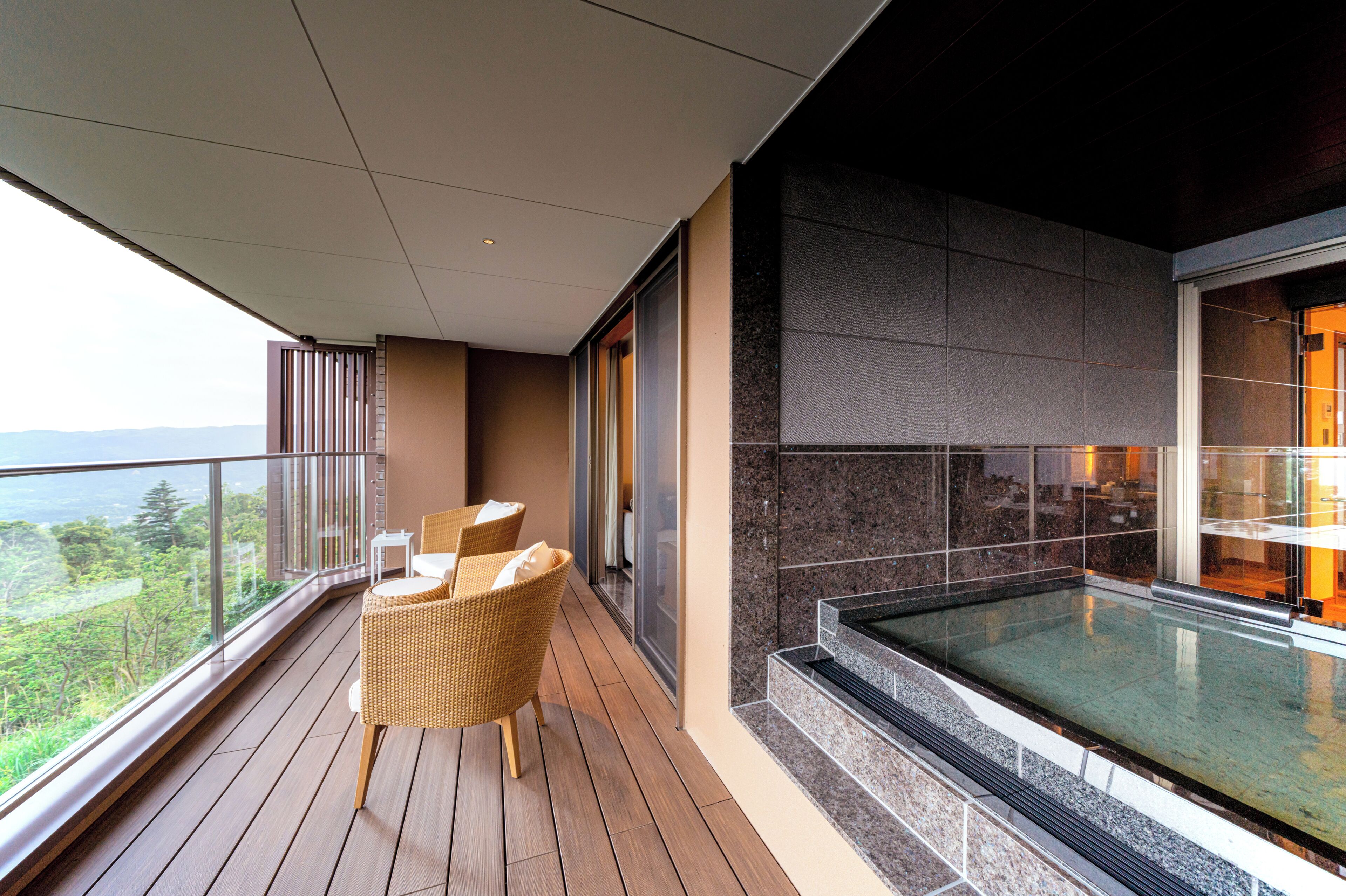 Un balcón con bañera de hidromasaje cubierta con vidrio, mobiliario de mimbre y vistas al exterior.