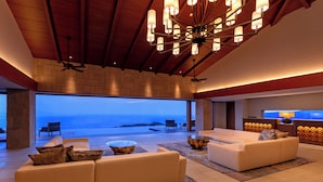 A spacious living area with a large sofa set, a coffee table, and a TV. The room features a high ceiling with exposed beams and a large window overlooking the ocean. - Izu Hotel Resort & Spa (Higashiizu)