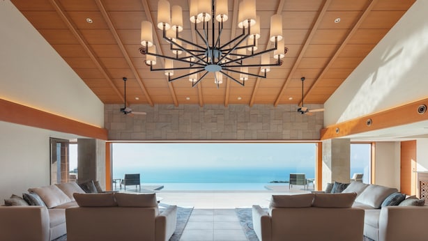 A spacious living area with a large, modern chandelier, a stone accent wall, and a view of the ocean. - Izu Hotel Resort & Spa (Higashiizu)
