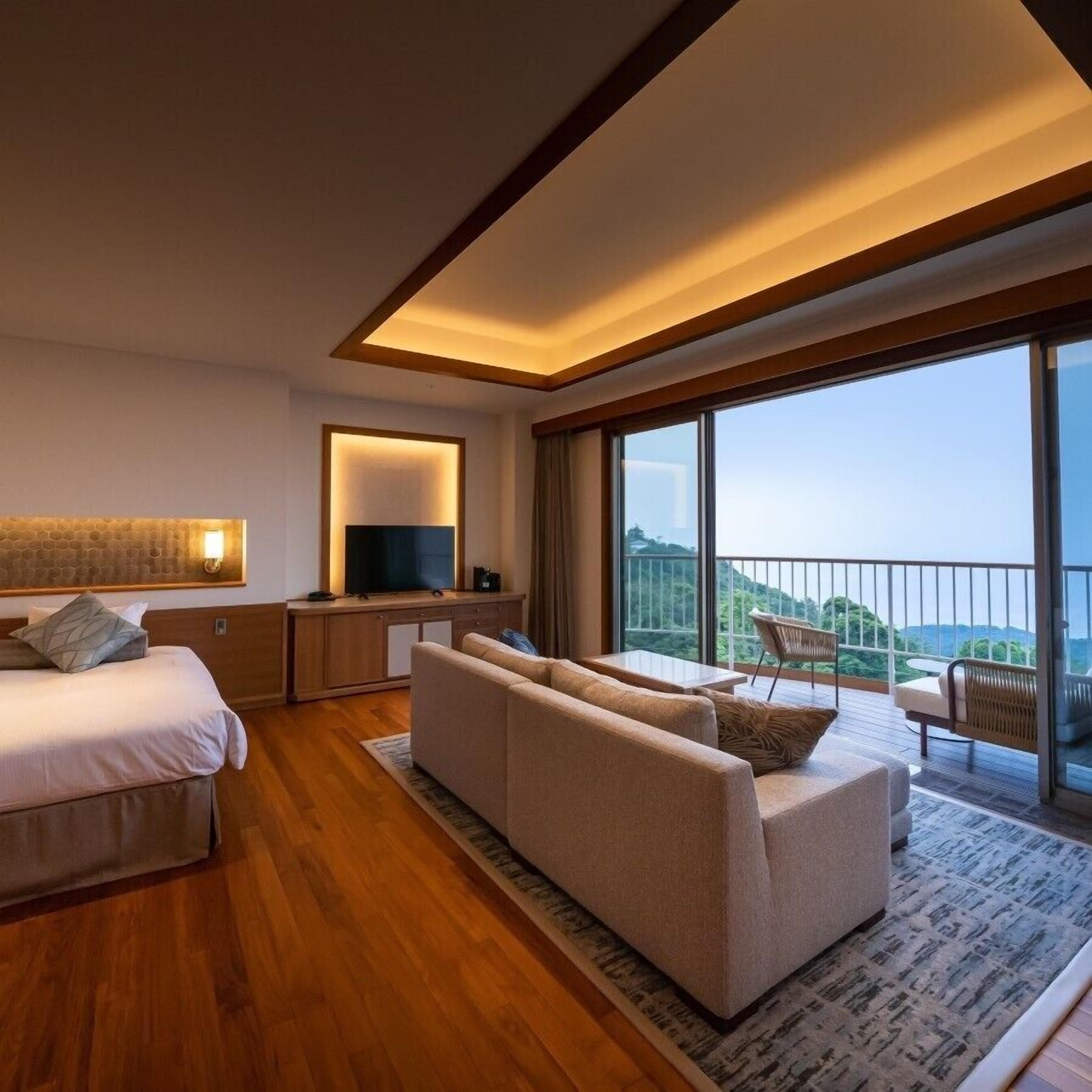 Una habitación de hotel moderna con una cama grande, un sofá, un televisor y un balcón con vistas.