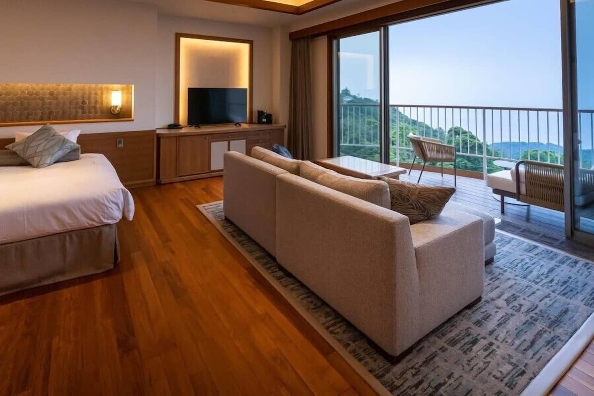 Una habitación de hotel moderna con una cama grande, un sofá, un televisor y un balcón con vistas.