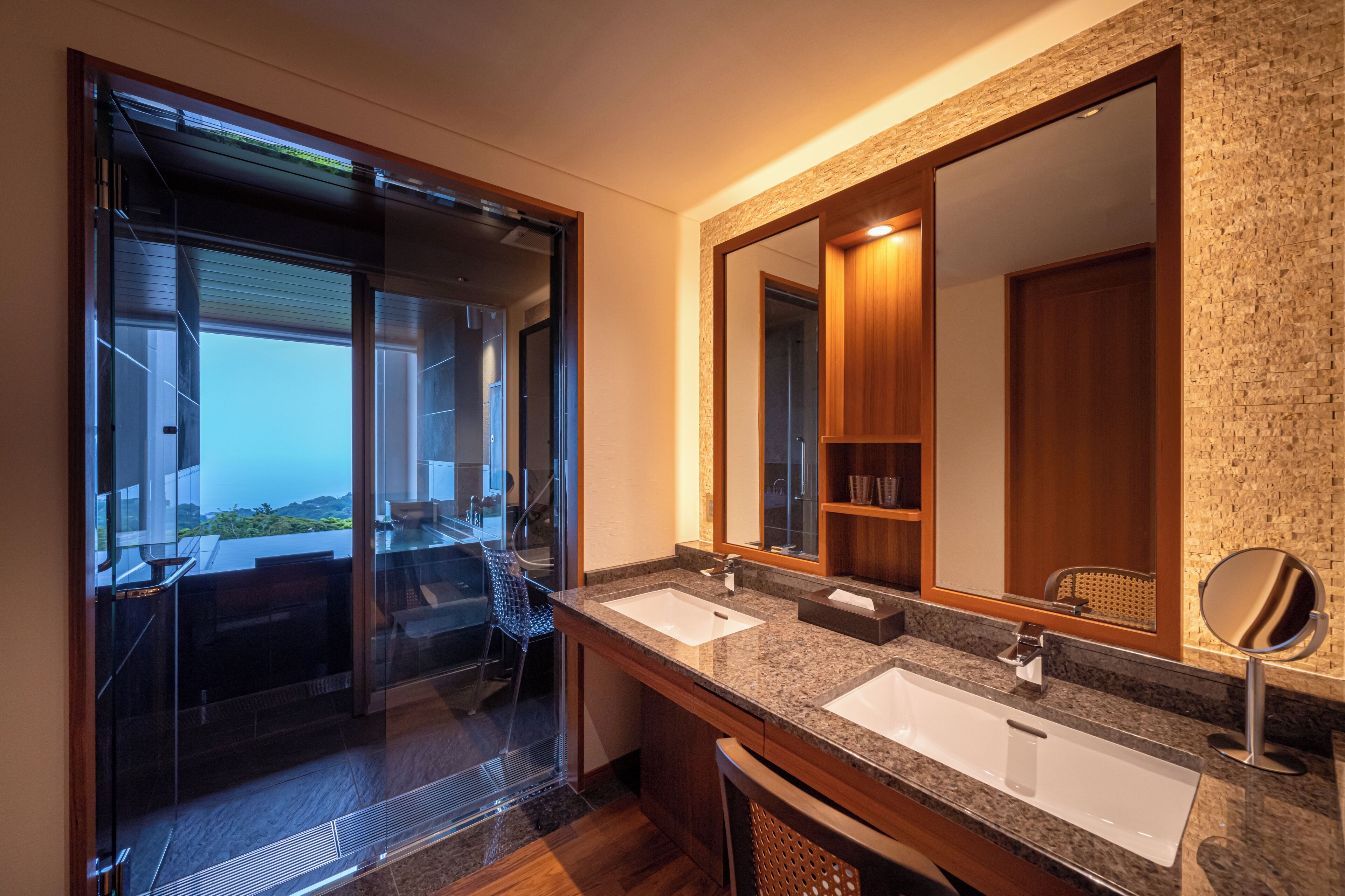 A modern bathroom with two sinks, a large mirror, and a glass door leading to a balcony.