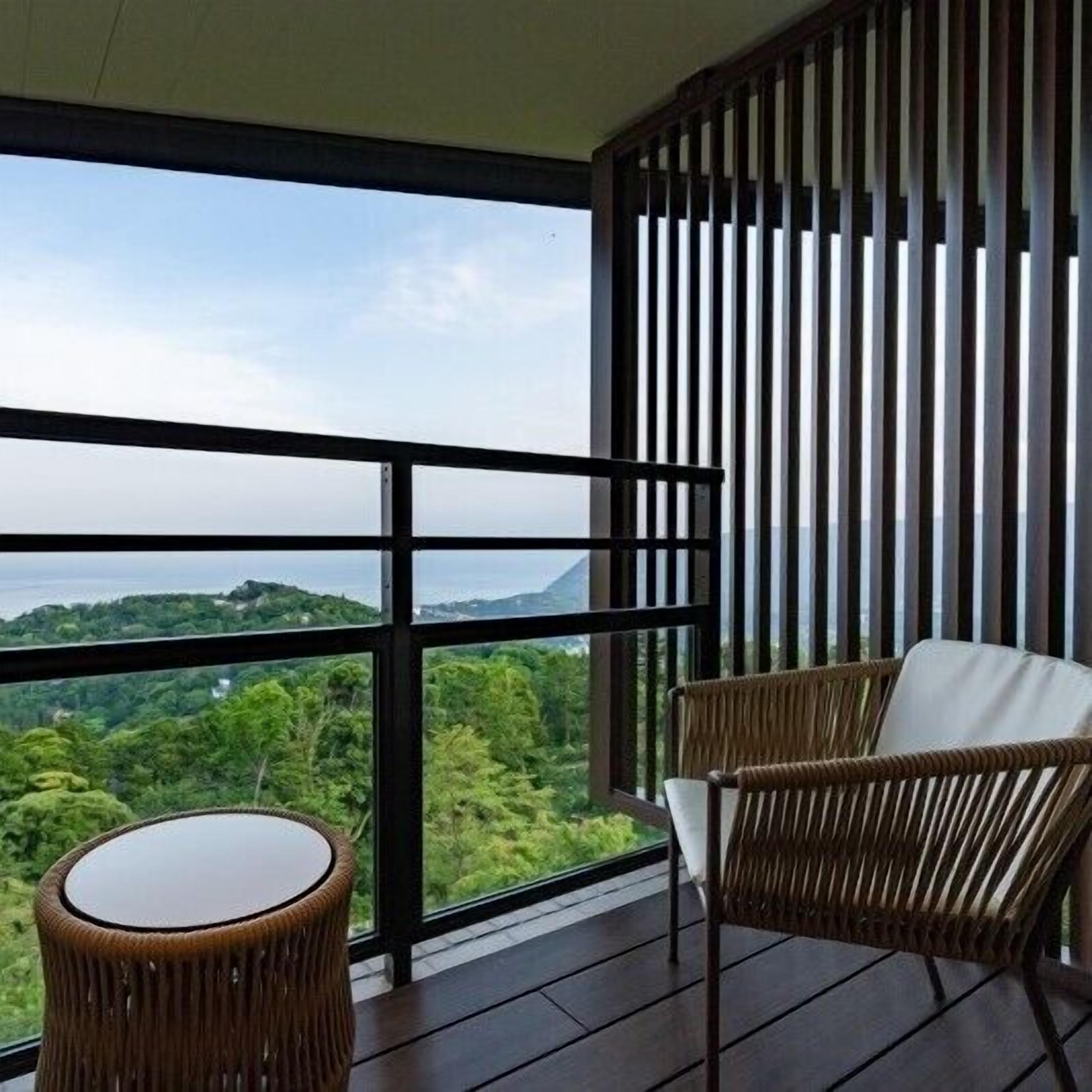 Un balcón con vistas a un paisaje montañoso, mobiliario de mimbre y barandilla de madera.