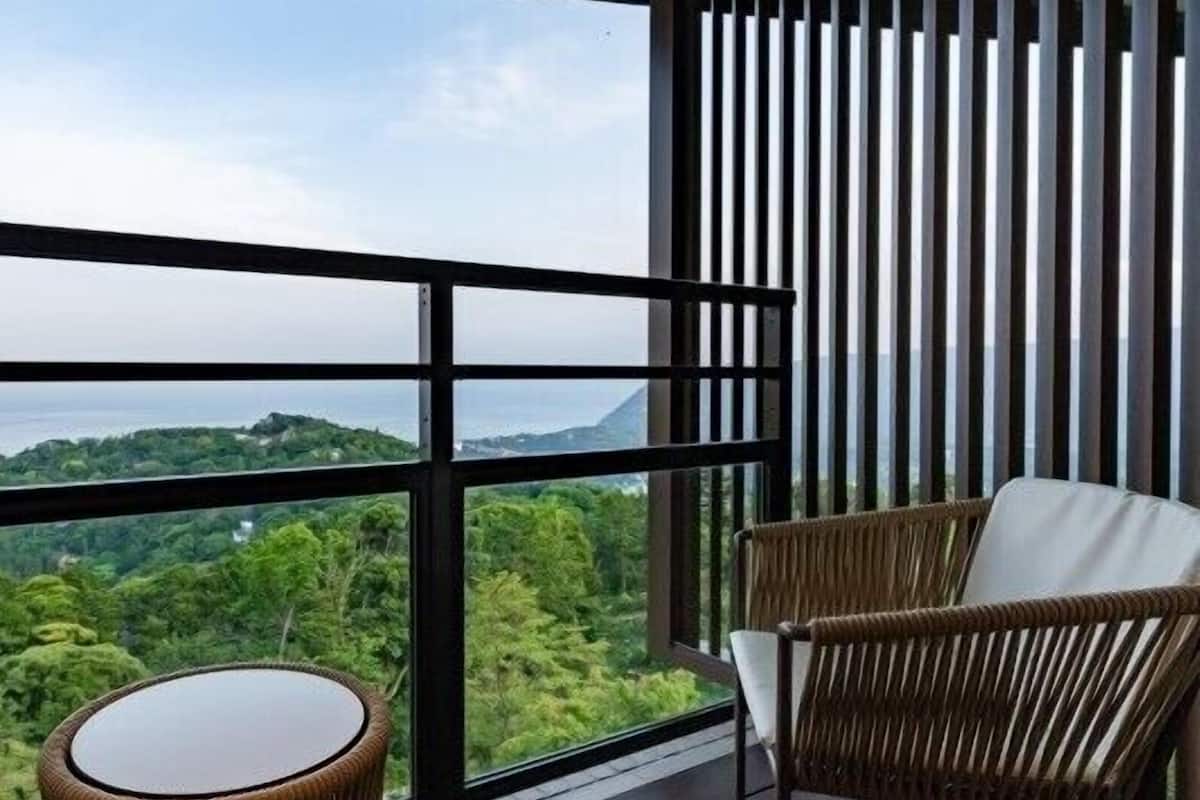 Un balcón con vistas a un paisaje montañoso, mobiliario de mimbre y barandilla de madera.