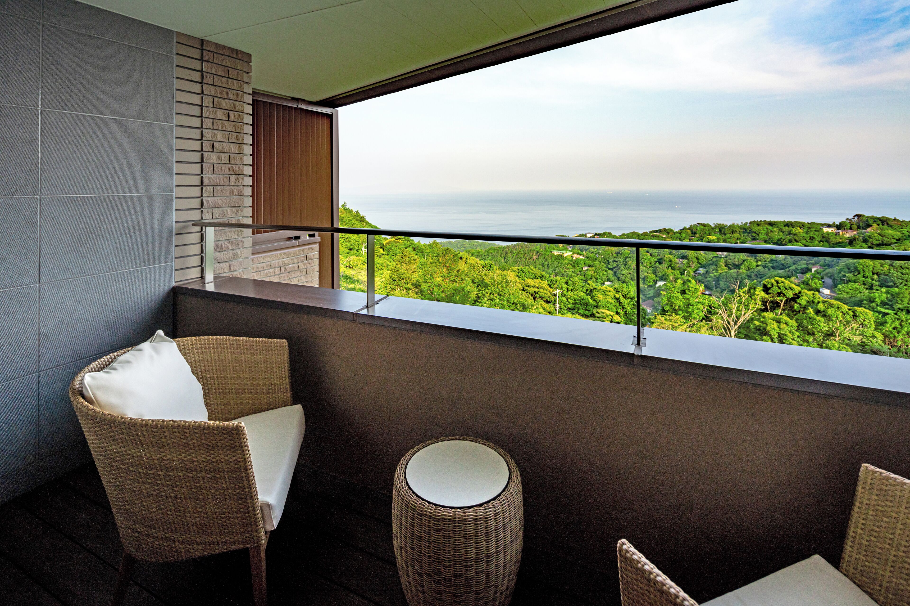 A balcony with wicker furniture, a view of the sea, and a brick wall.