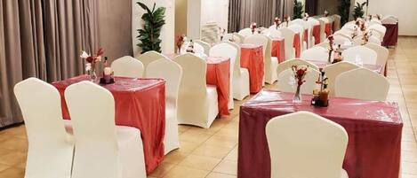 A banquet hall with rows of round tables covered with red tablecloths and white chairs.