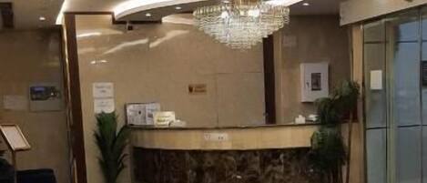 A hotel lobby with a reception desk, seating area, and a chandelier.