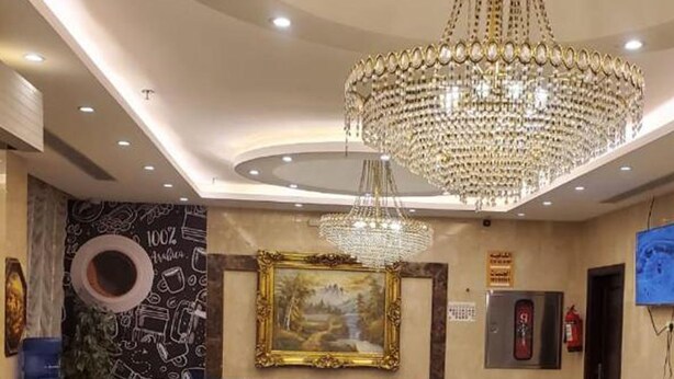 A lobby with a large chandelier, a blue sofa set, a framed painting, and a water feature. - Taj Al Zahabiya Hotel (Makkah)