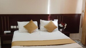 A hotel room with a large bed, two white pillows, a gold throw blanket, and a wooden headboard. - Taj Al Zahabiya Hotel (Makkah)